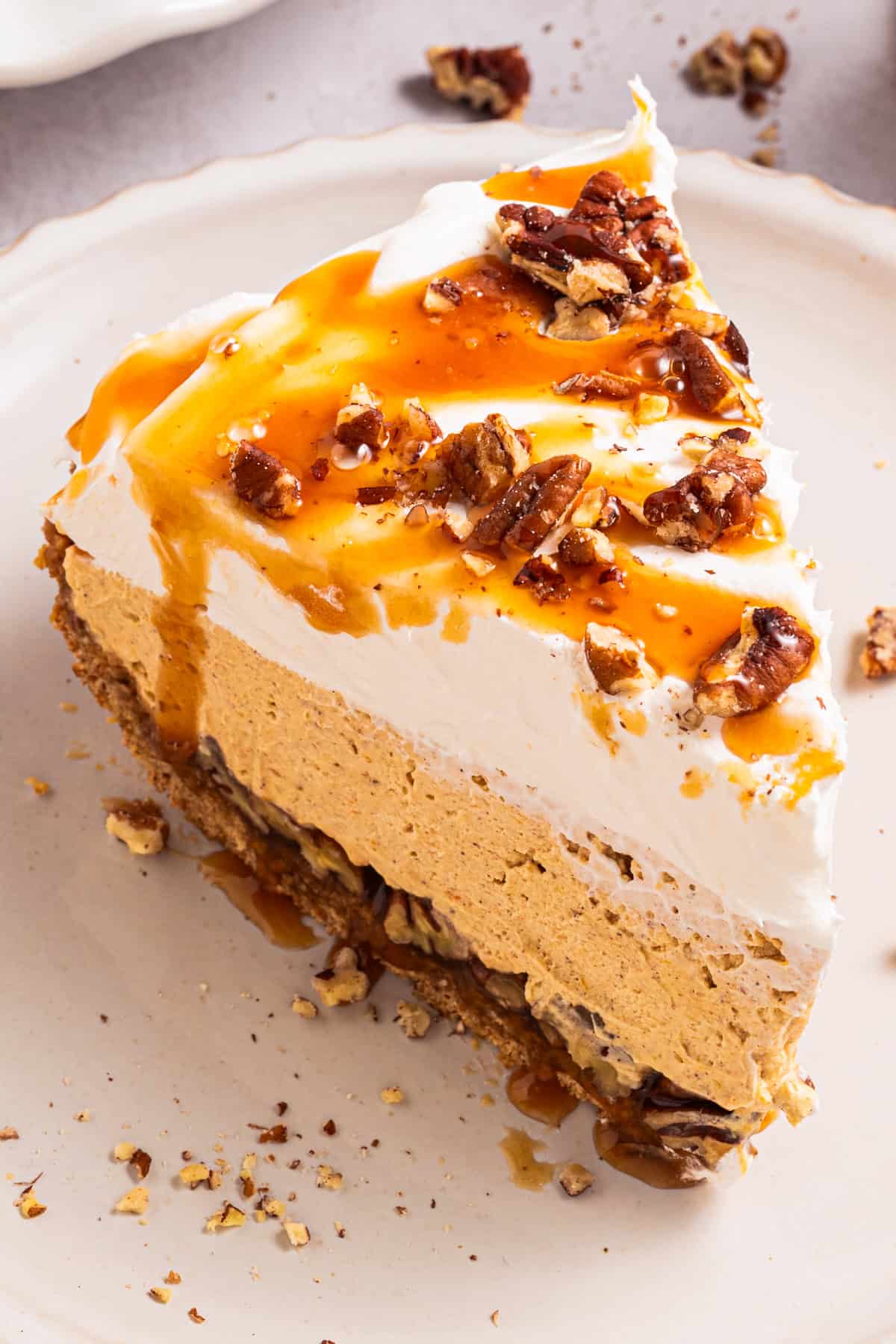 Turtle Pumpkin Pie A slice of layered pumpkin pie topped with whipped cream, caramel sauce, and chopped pecans sits on a white plate.