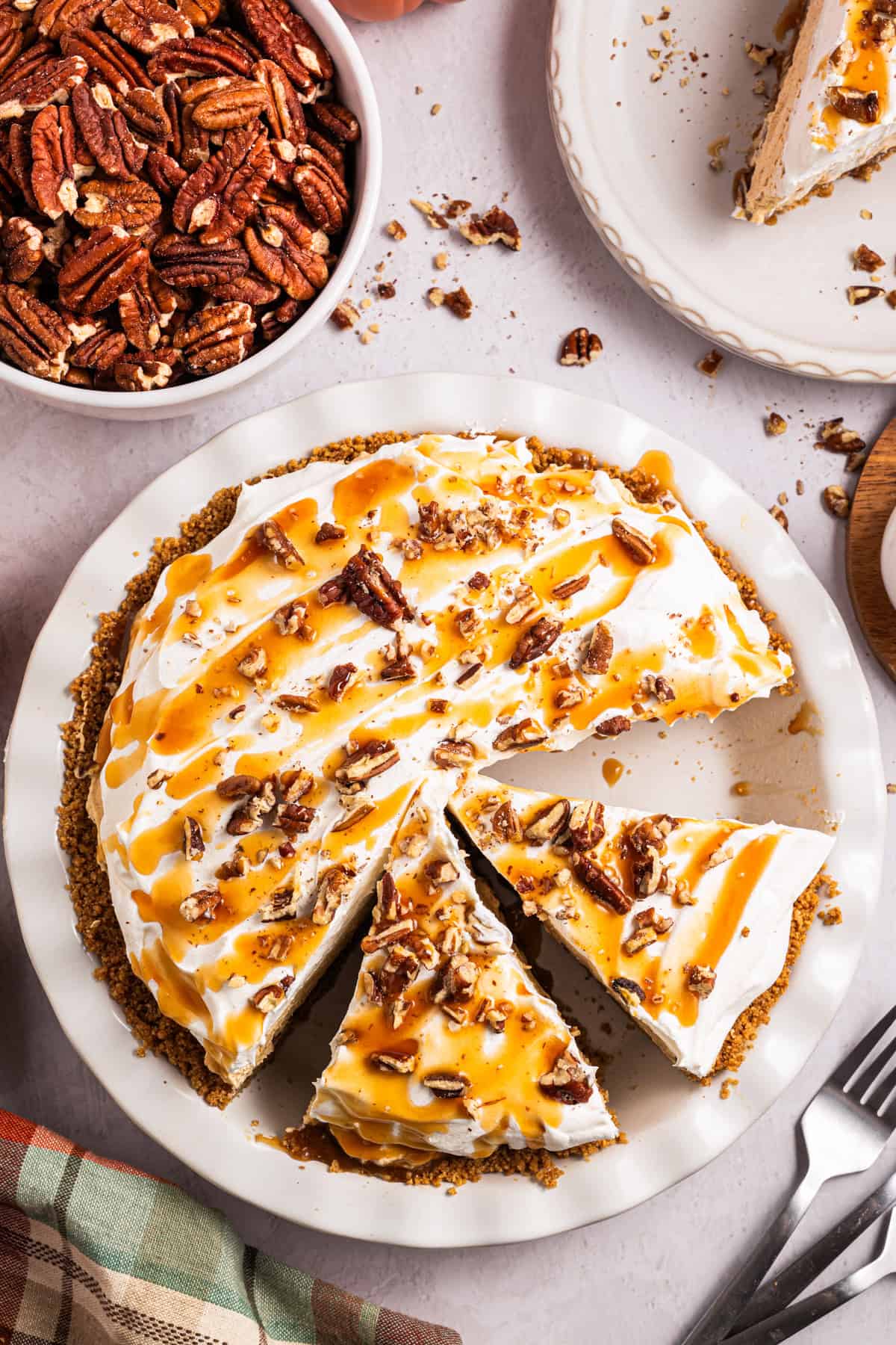 Turtle Pumpkin Pie A pie topped with whipped cream, chopped pecans, and caramel sauce sits on a table.
