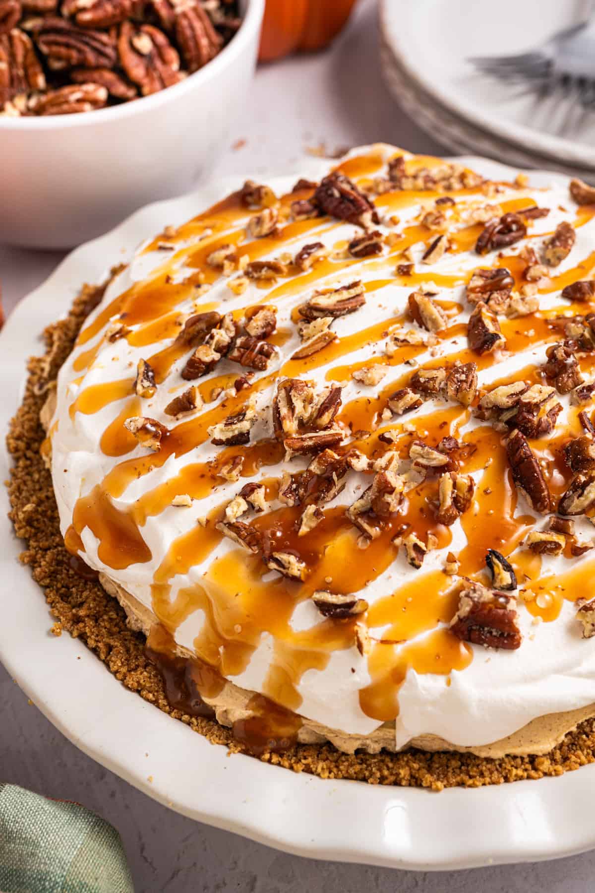 Turtle Pumpkin Pie A pie with a graham cracker crust, topped with whipped cream, chopped pecans, and caramel drizzle.