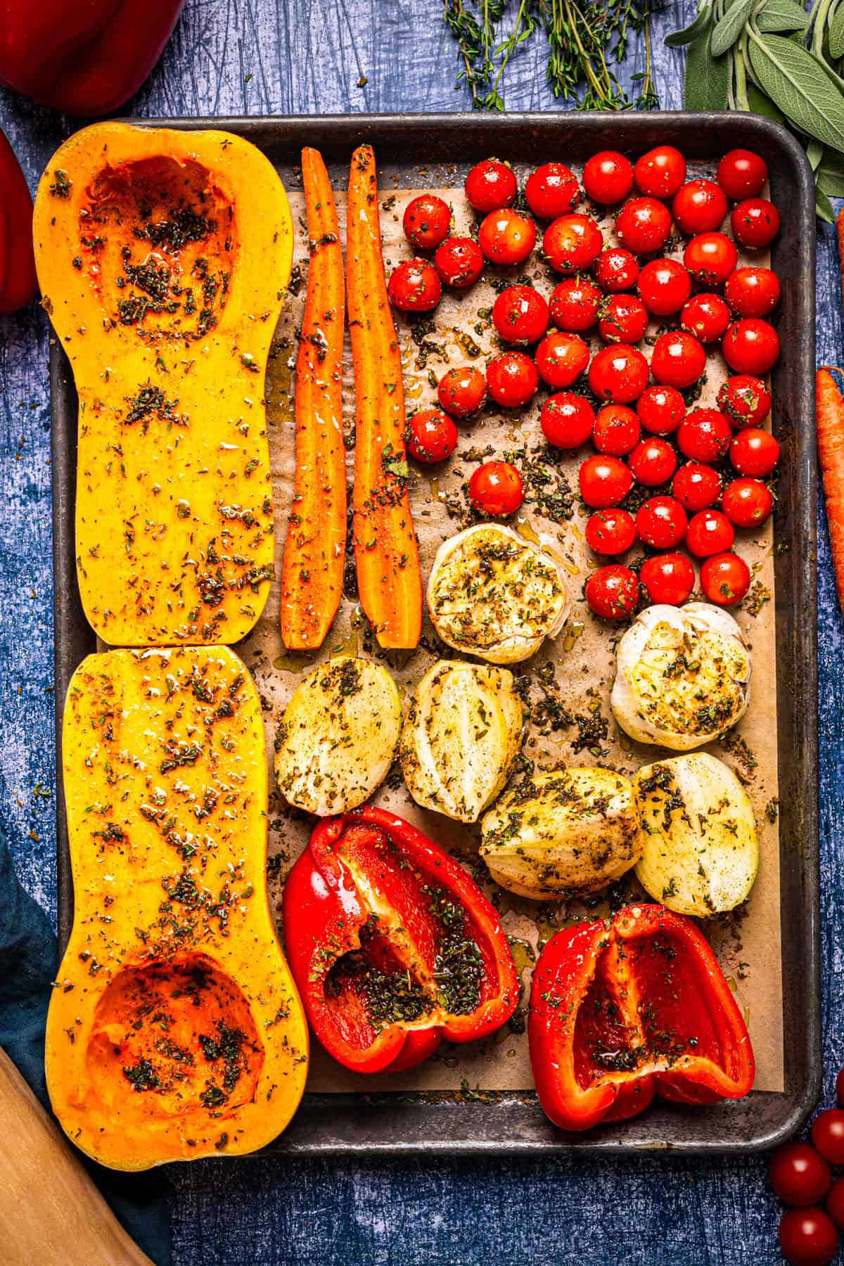 Butternut Squash Soup A baking sheet filled with seasoned butternut squash halves, carrots, cherry tomatoes, heads of garlic, and red bell pepper halves.