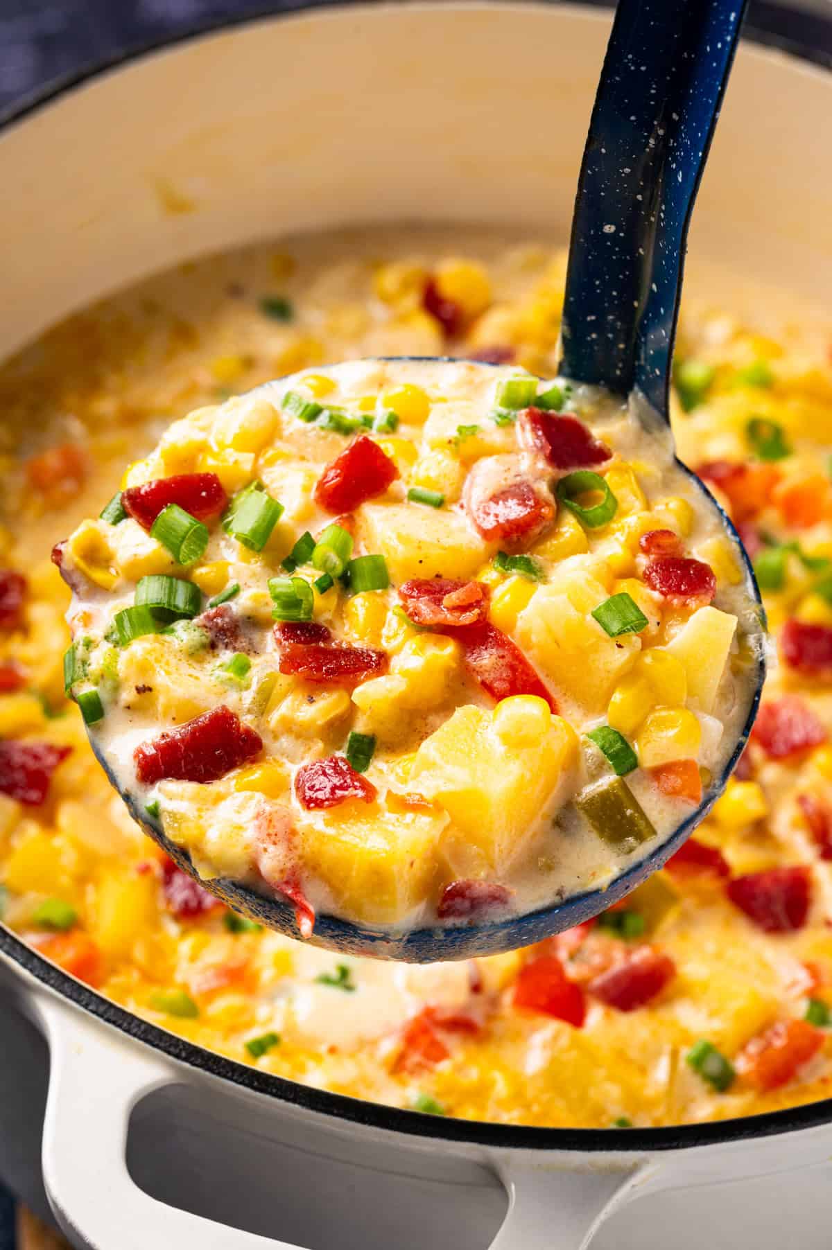 Corn Chowder with Bacon and Potatoes (One Pot) A ladle filled with creamy corn chowder topped with bacon, diced red peppers, and chopped green onions.