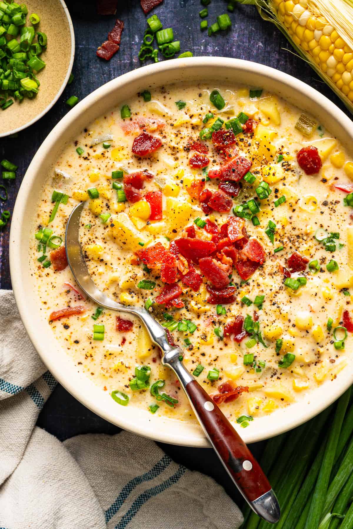 Corn Chowder with Bacon and Potatoes (One Pot) A bowl of creamy corn chowder topped with bacon and chopped green onions, with a spoon resting in the bowl.