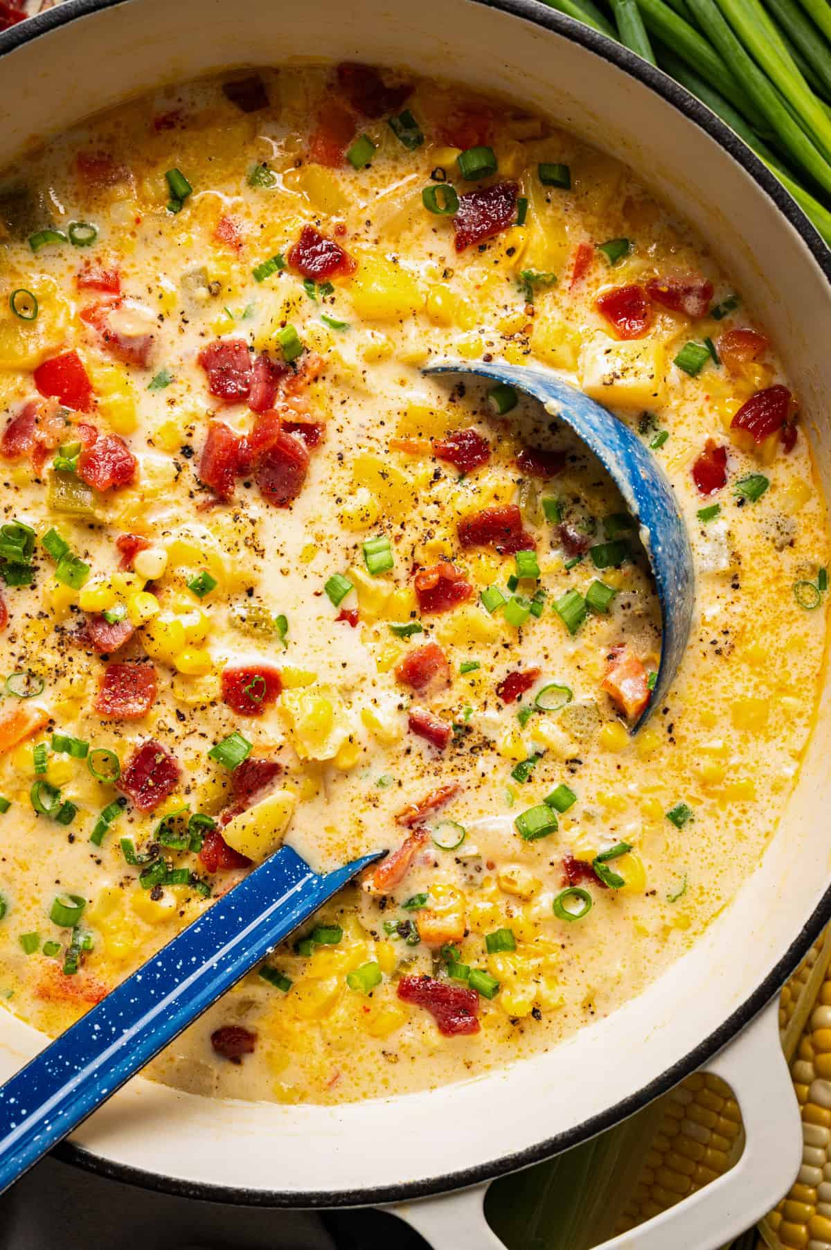 Corn Chowder with Bacon and Potatoes (One Pot) Creamy corn chowder with bacon and green onions in a large pot with a blue ladle.