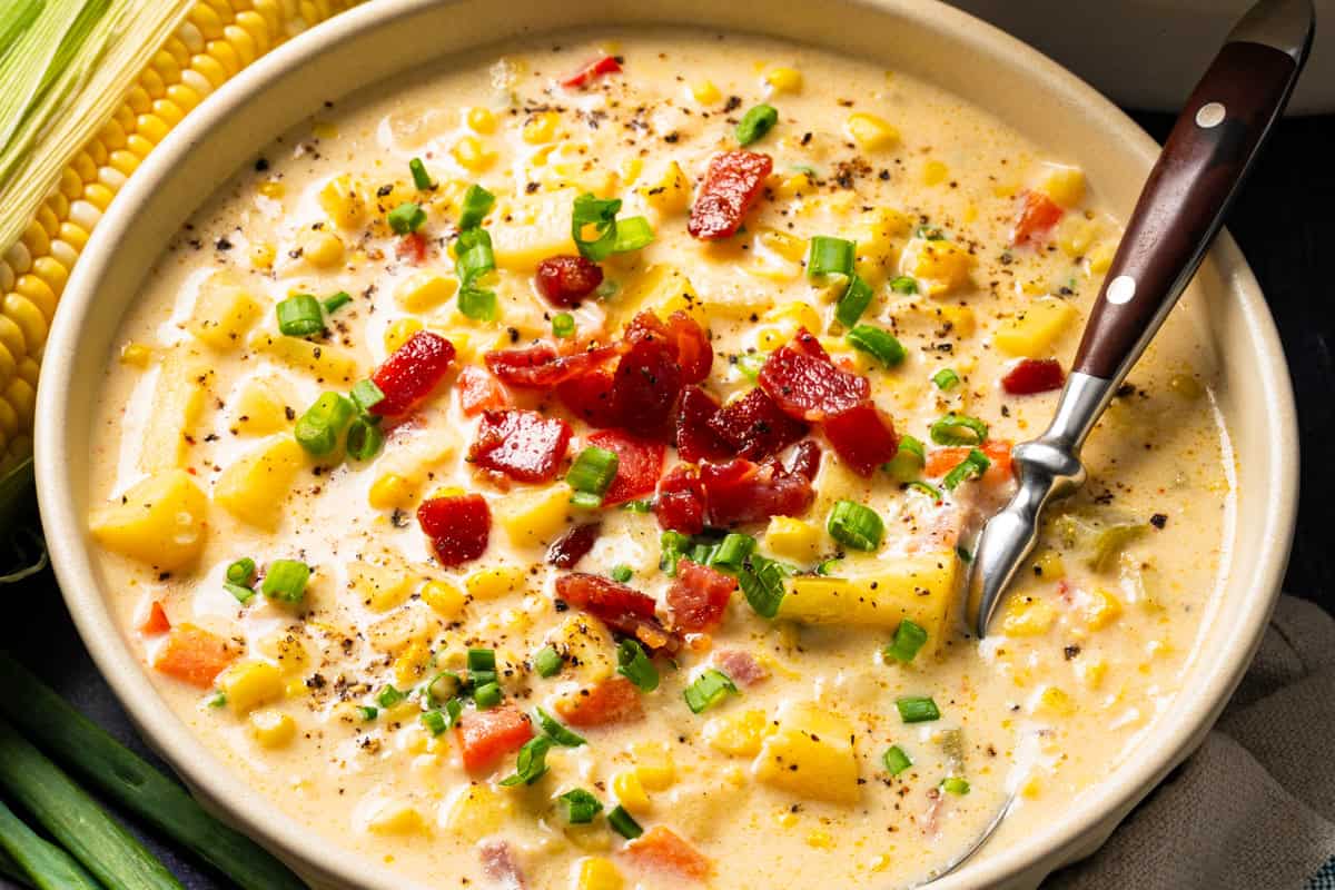 Corn Chowder with Bacon and Potatoes (One Pot) A bowl of creamy corn and potato chowder topped with bacon bits and green onions, served with a spoon.