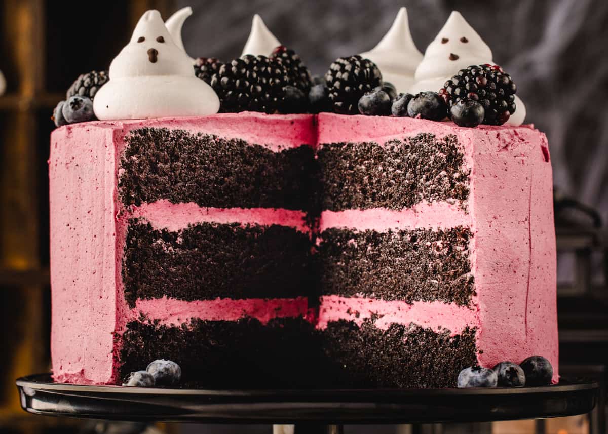 Halloween Cake A layer chocolate cake with pink frosting, topped with meringue ghosts, blackberries, and blueberries, with one slice removed.