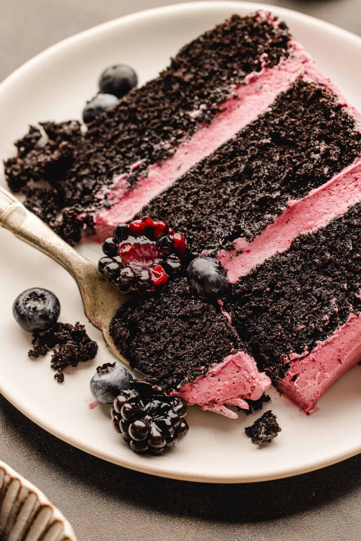 Halloween Cake A slice of chocolate layer cake with pink filling on a white plate, topped with fresh blackberries and blueberries.