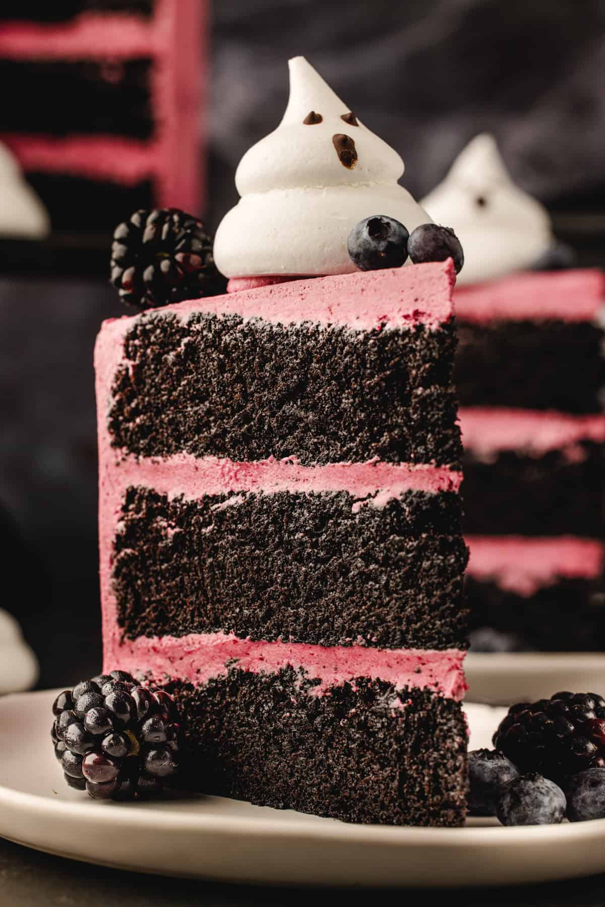 Halloween Cake A slice of three-layer chocolate cake with pink frosting, topped with a ghost-shaped meringue and fresh blackberries and blueberries.