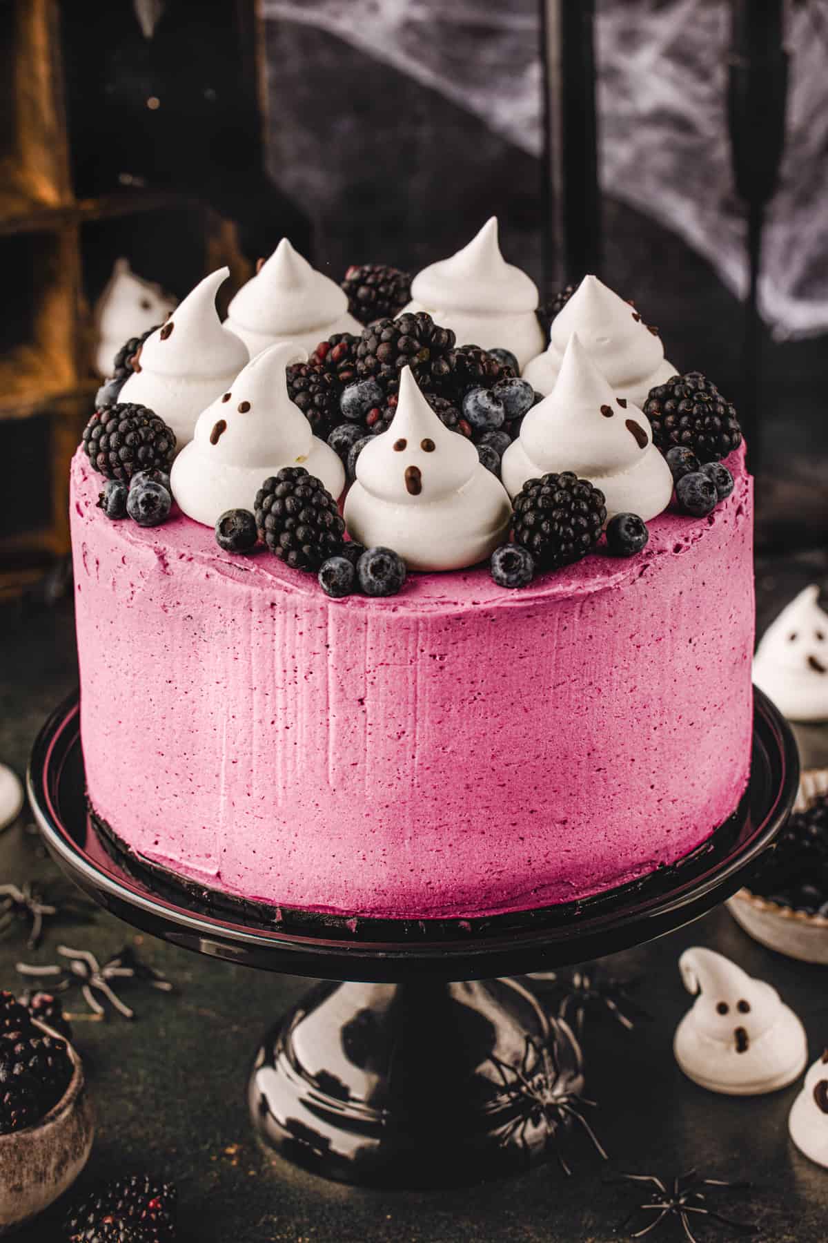 Halloween Cake A round cake with bright pink frosting topped with blackberries, blueberries, and meringue ghosts.