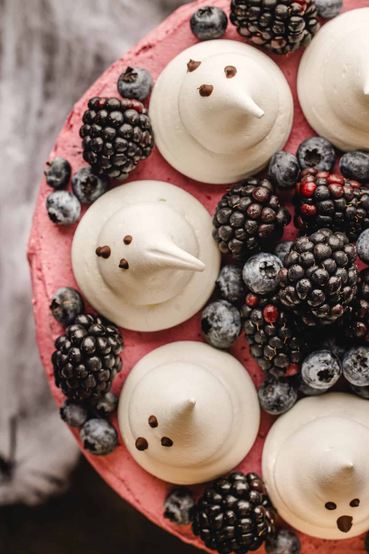 Halloween Cake Top-down view of a pink frosted cake decorated with blackberries, blueberries, and meringue cookies shaped like ghosts.