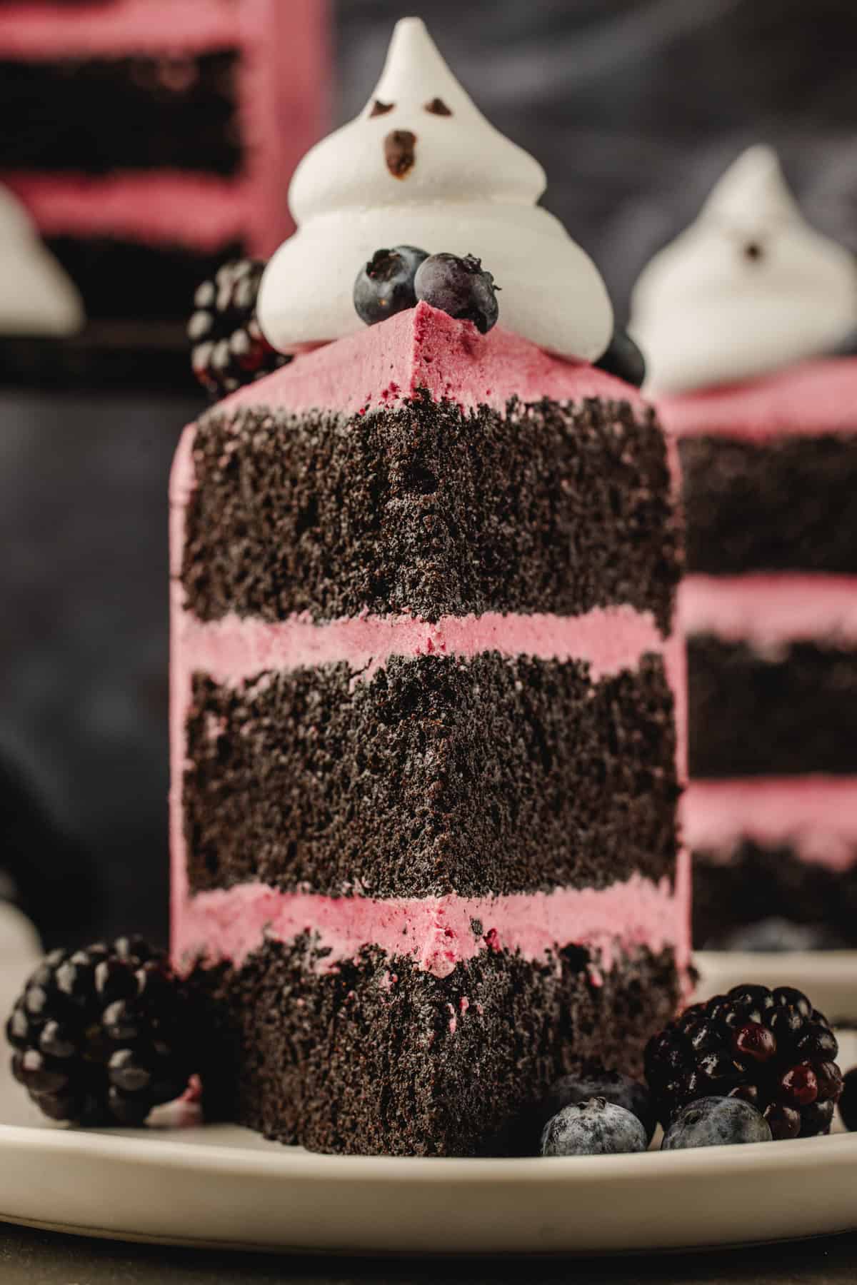 Halloween Cake A slice of three-layered chocolate cake with pink frosting, topped with a meringue ghost and fresh berries.