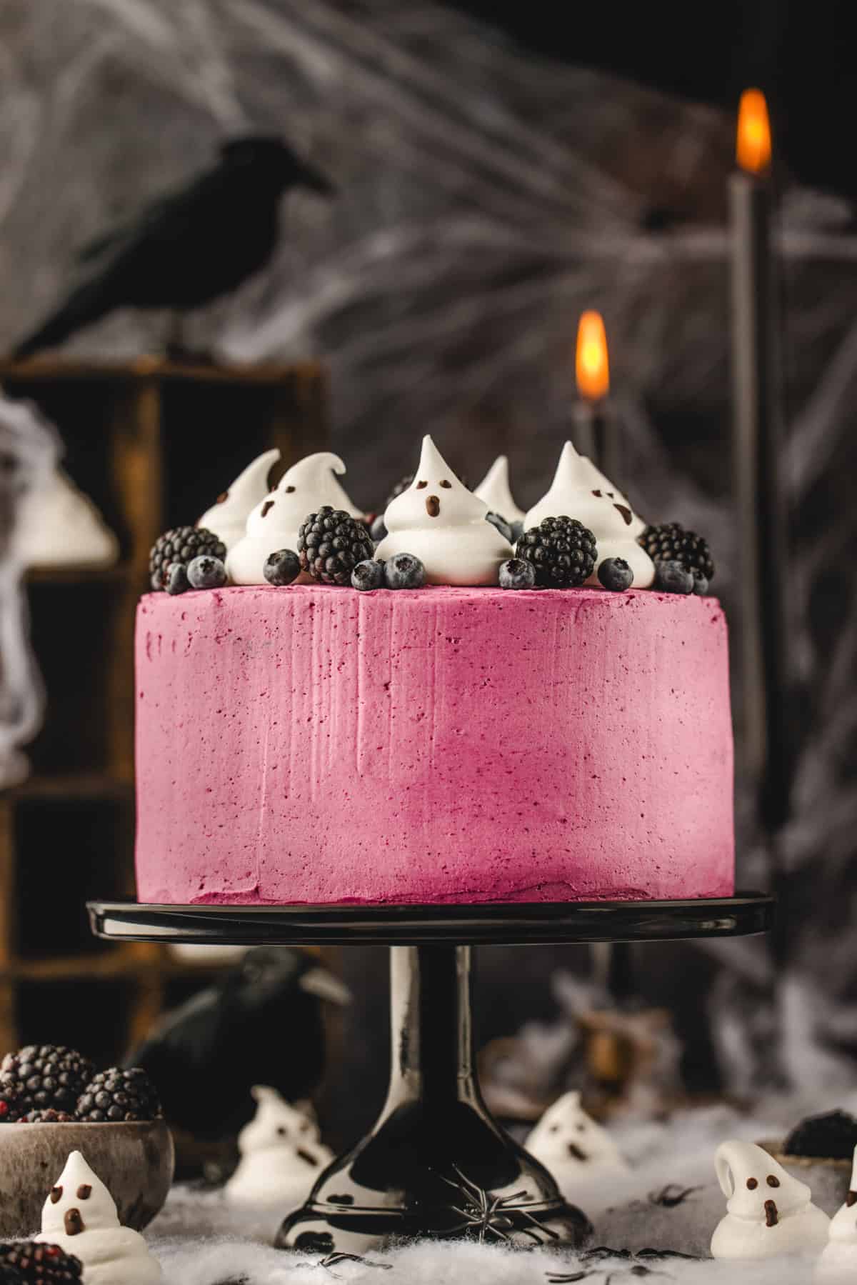 Halloween Cake A round pink frosted cake on a stand, decorated with meringue ghosts, blueberries, and blackberries.
