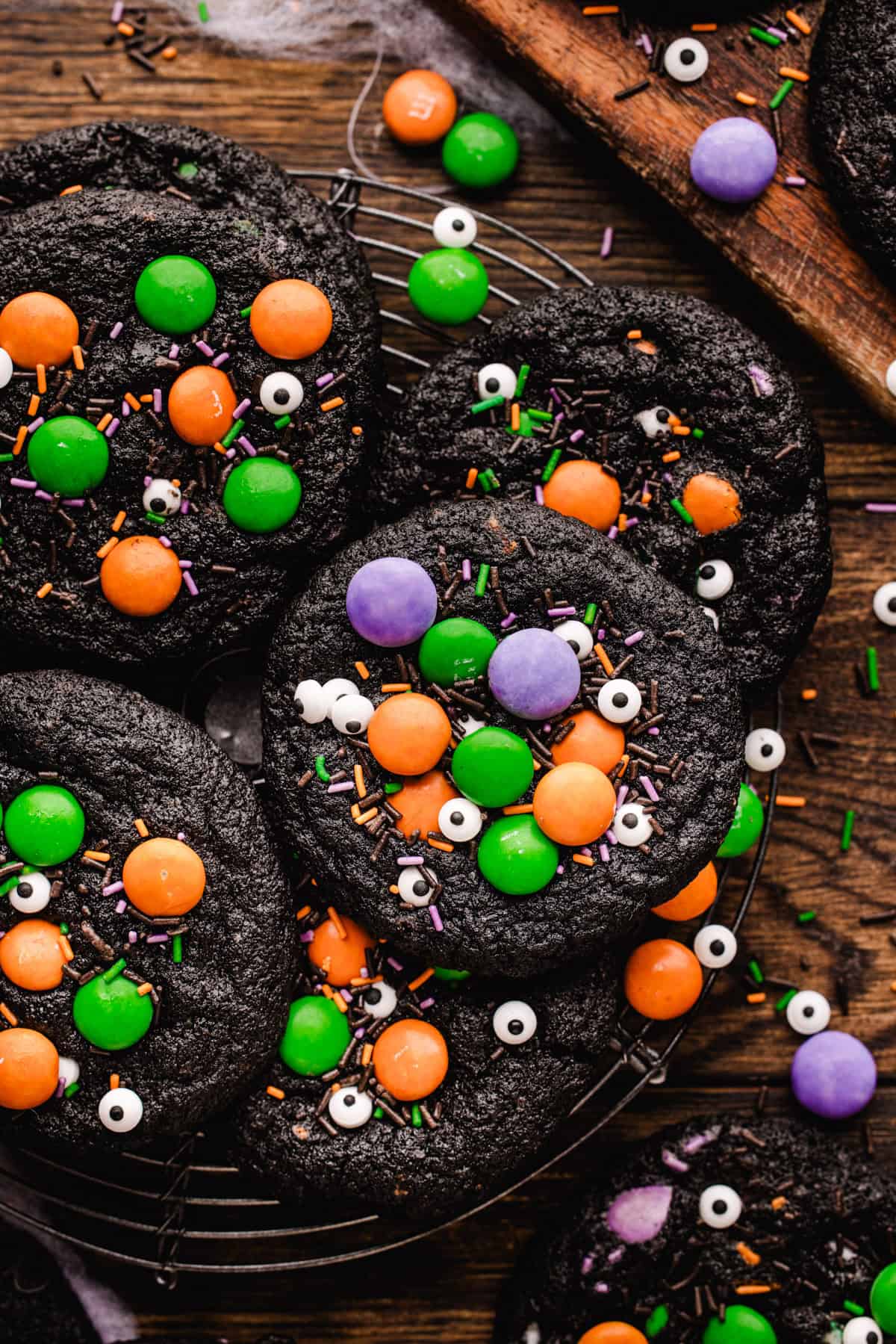 Halloween Cookies Black chocolate cookies decorated with colorful candy-coated chocolates, candy eyeballs, and sprinkles on a wire cooling rack.