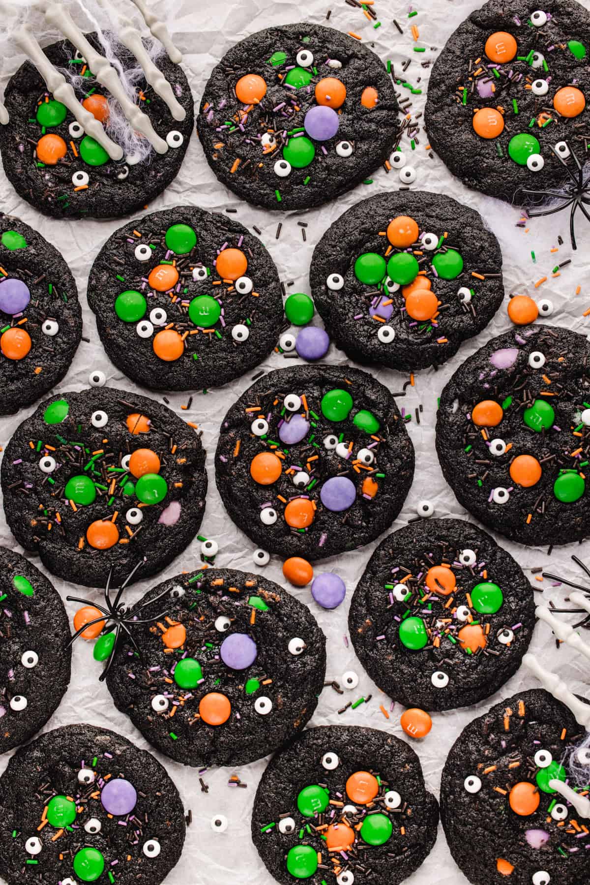 Halloween Cookies Black chocolate cookies decorated with colorful candy-coated chocolates, sprinkles, and candy eyeballs on white parchment paper.