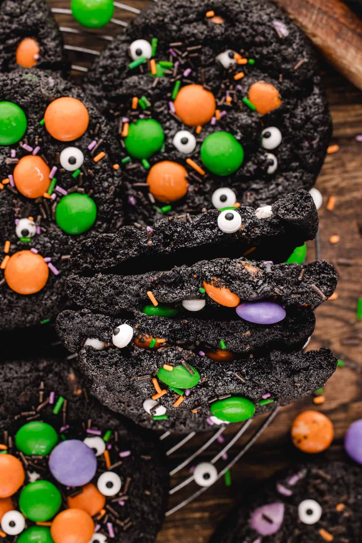 Halloween Cookies Black cocoa cookies decorated with colorful candy-coated chocolates, candy eyes, and sprinkles on a wire cooling rack.