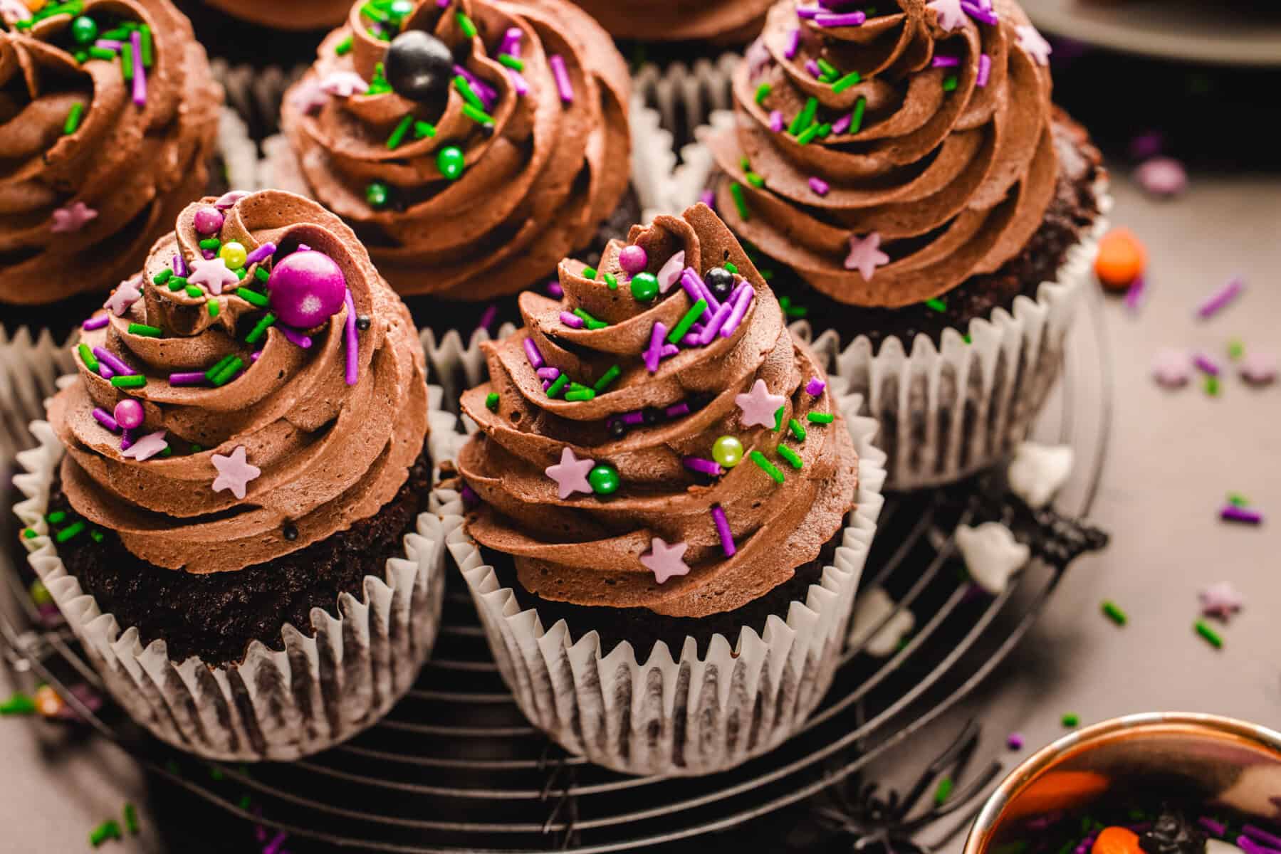 Halloween Cupcakes Chocolate cupcakes with swirled frosting and colorful star and sphere-shaped sprinkles on a wire cooling rack.