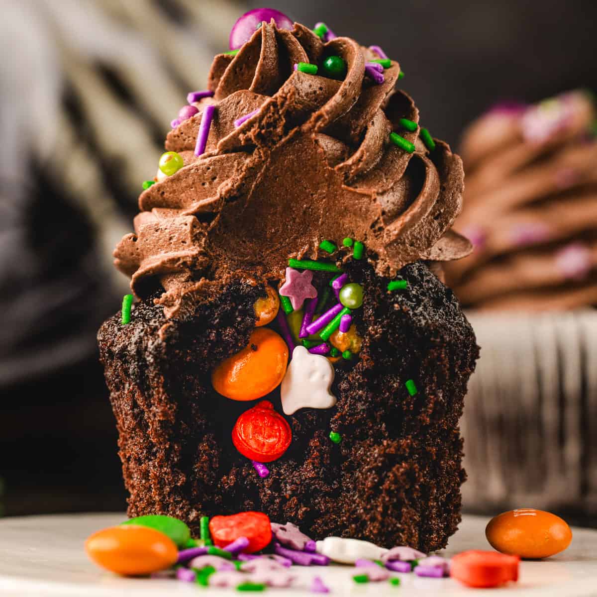 Halloween Cupcakes A chocolate cupcake with a large bite taken out, revealing a center filled with colorful candies, sprinkles, and a ghost-shaped sweet.