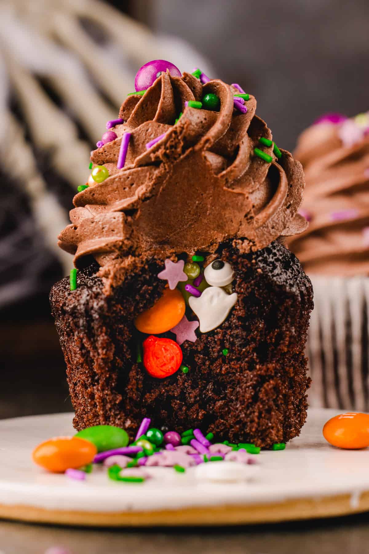 Halloween Cupcakes Chocolate cupcake with a bite taken out, revealing a hidden filling of assorted Halloween-themed sprinkles, including a ghost and eyeball.