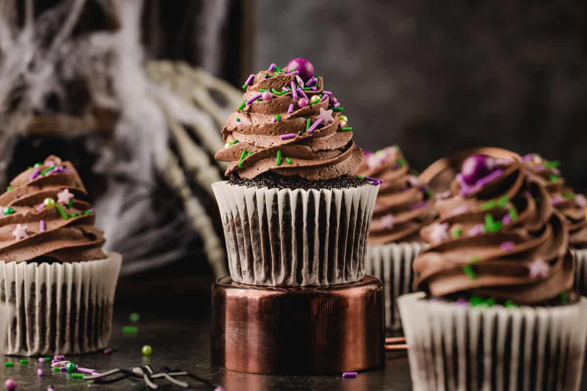 Halloween Cupcakes Chocolate cupcakes topped with chocolate frosting and festive purple, green, and gold sprinkles.