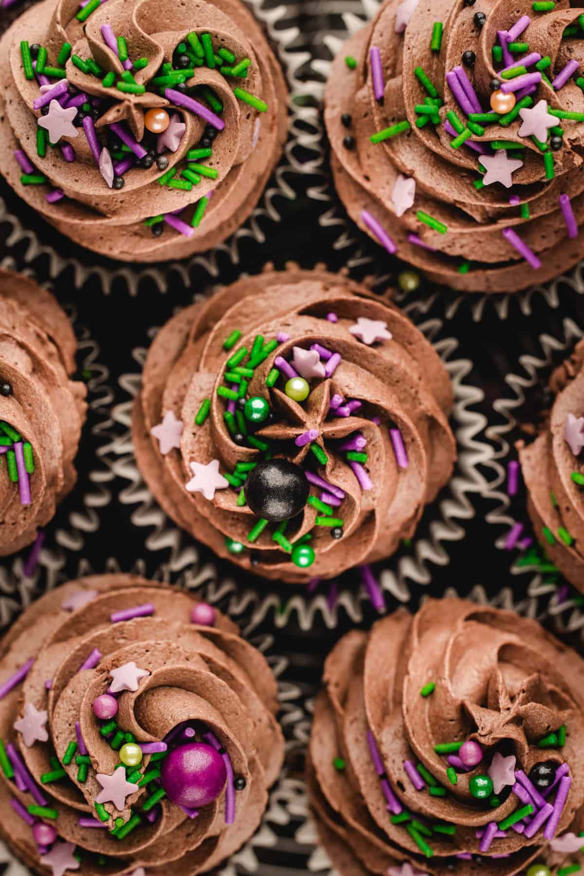 Halloween Cupcakes Top-down view of chocolate cupcakes topped with chocolate frosting, star-shaped sprinkles, and colorful round sprinkles.