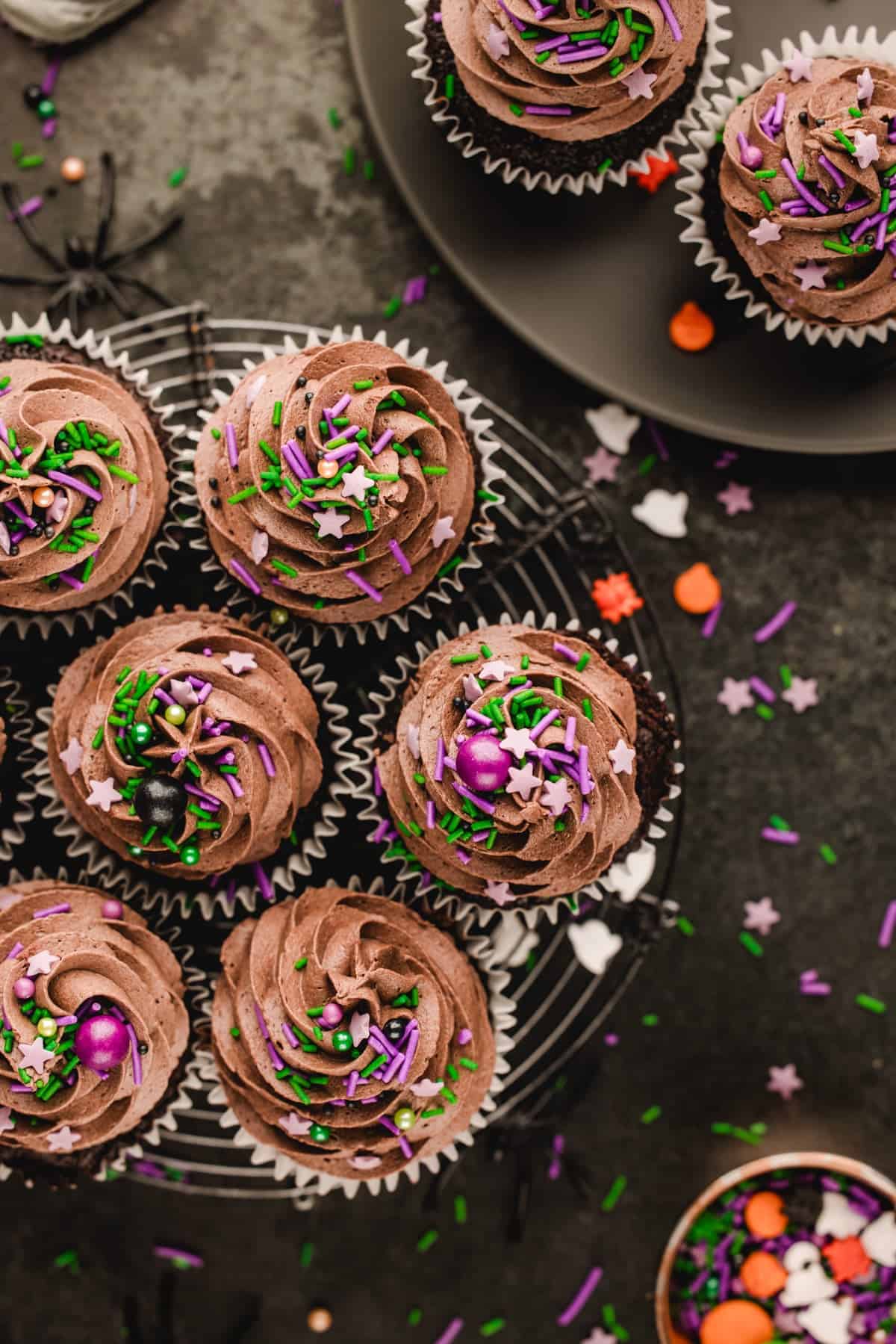 Halloween Cupcakes Chocolate cupcakes with chocolate frosting and Halloween-themed sprinkles on a wire cooling rack and plate.