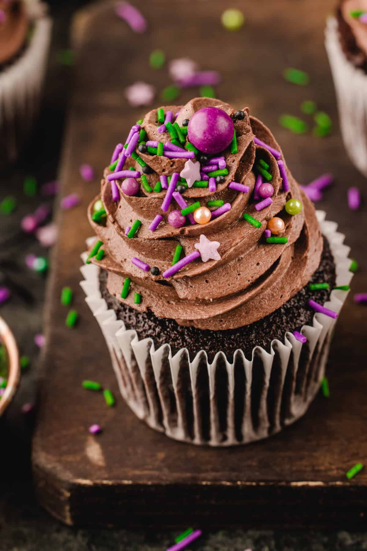 Halloween Cupcakes A chocolate cupcake with chocolate frosting topped with purple and green sprinkles and star-shaped candies.