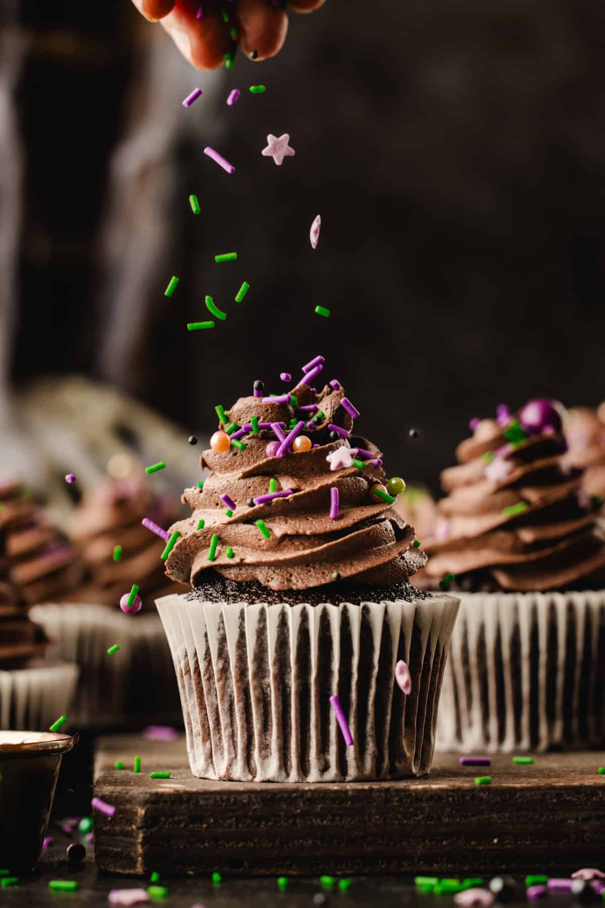 Halloween Cupcakes Hand sprinkling colorful star and rod-shaped sprinkles over a chocolate-frosted cupcake.