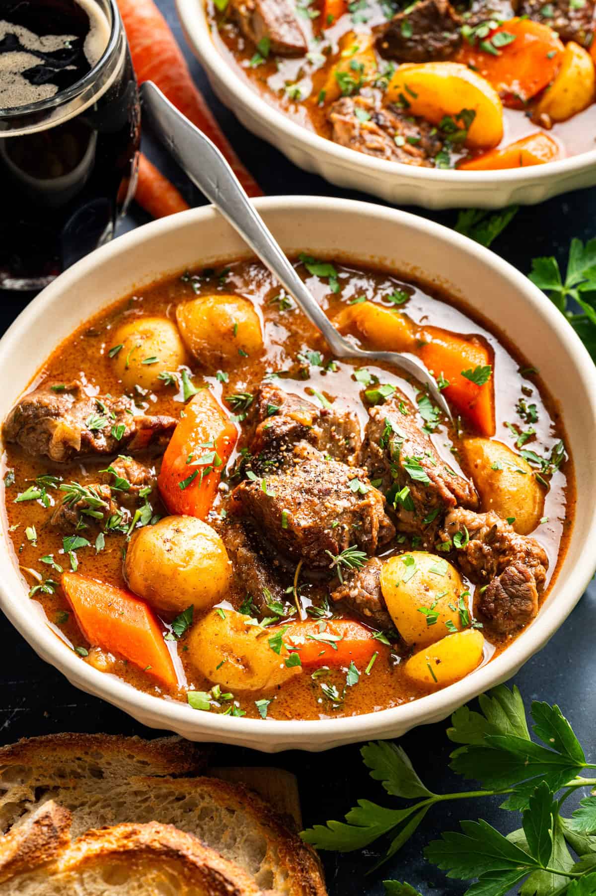 Irish Beef Stew A bowl of beef stew with chunks of meat, potatoes, and carrots, garnished with fresh herbs, with a spoon resting inside.