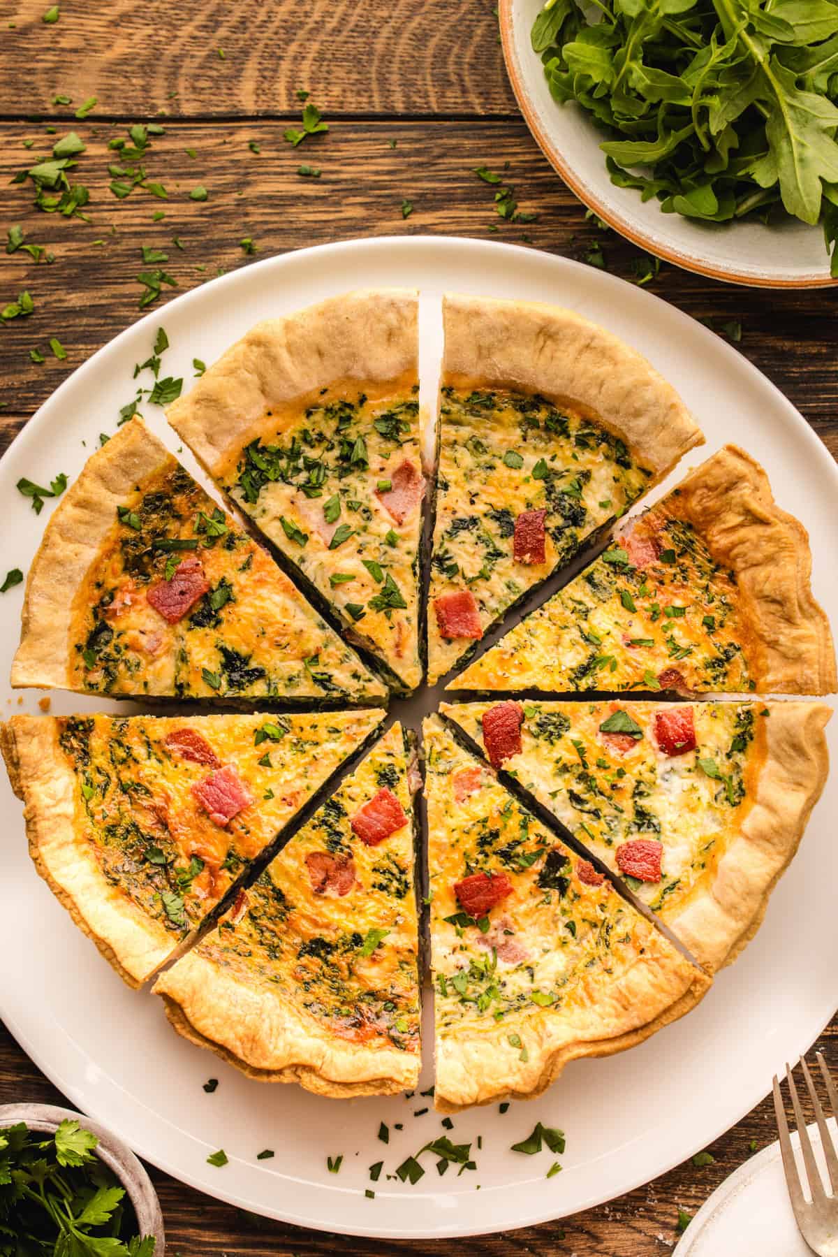 Quiche A sliced quiche with bacon and greens on a white plate.