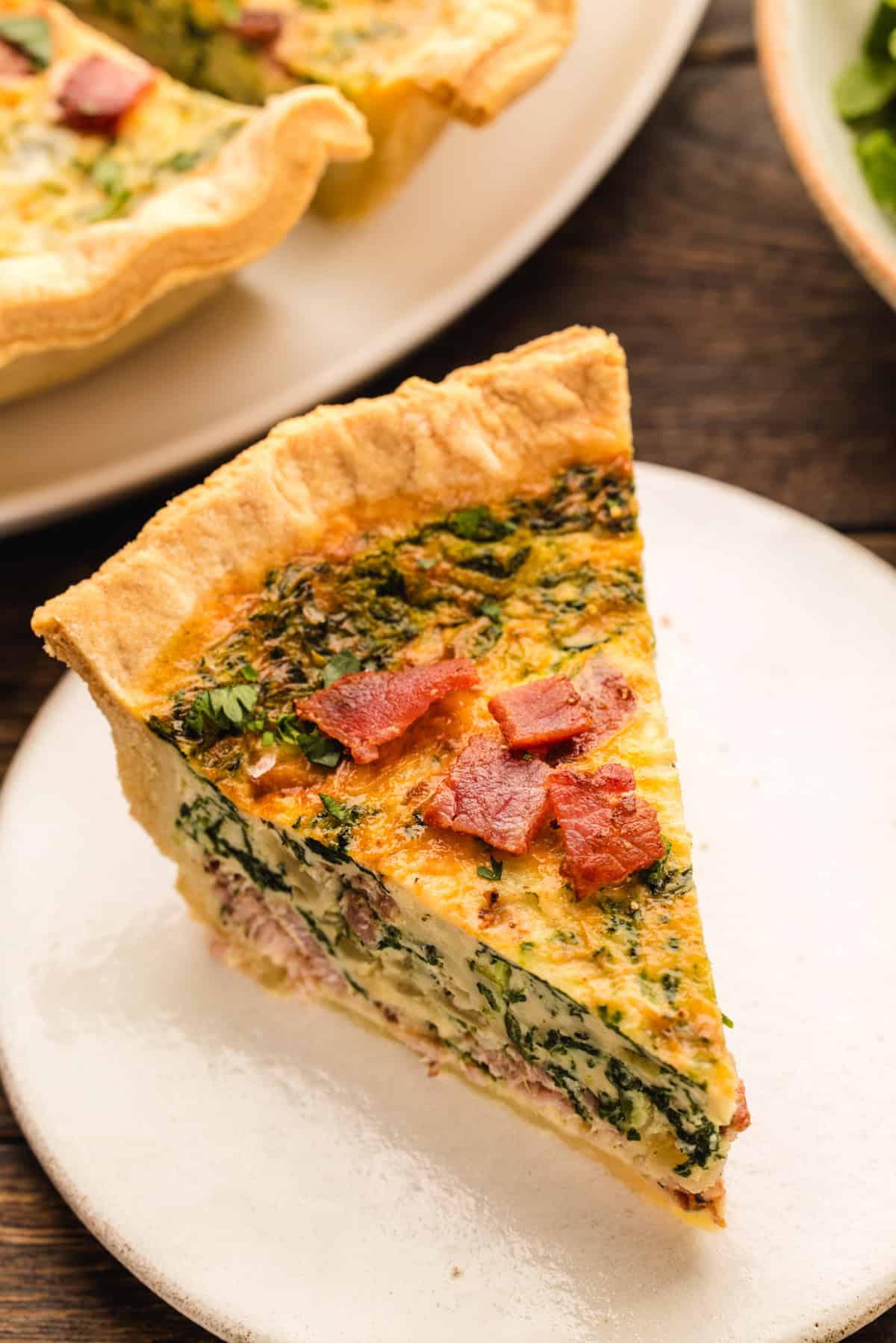 Quiche A slice of spinach and bacon quiche on a white plate.