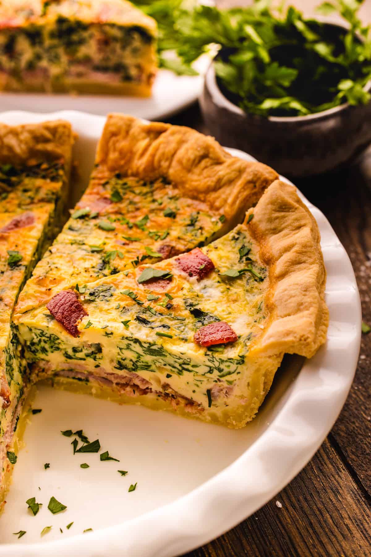Quiche A slice of quiche with spinach, and bacon in a fluted white ceramic pie dish.
