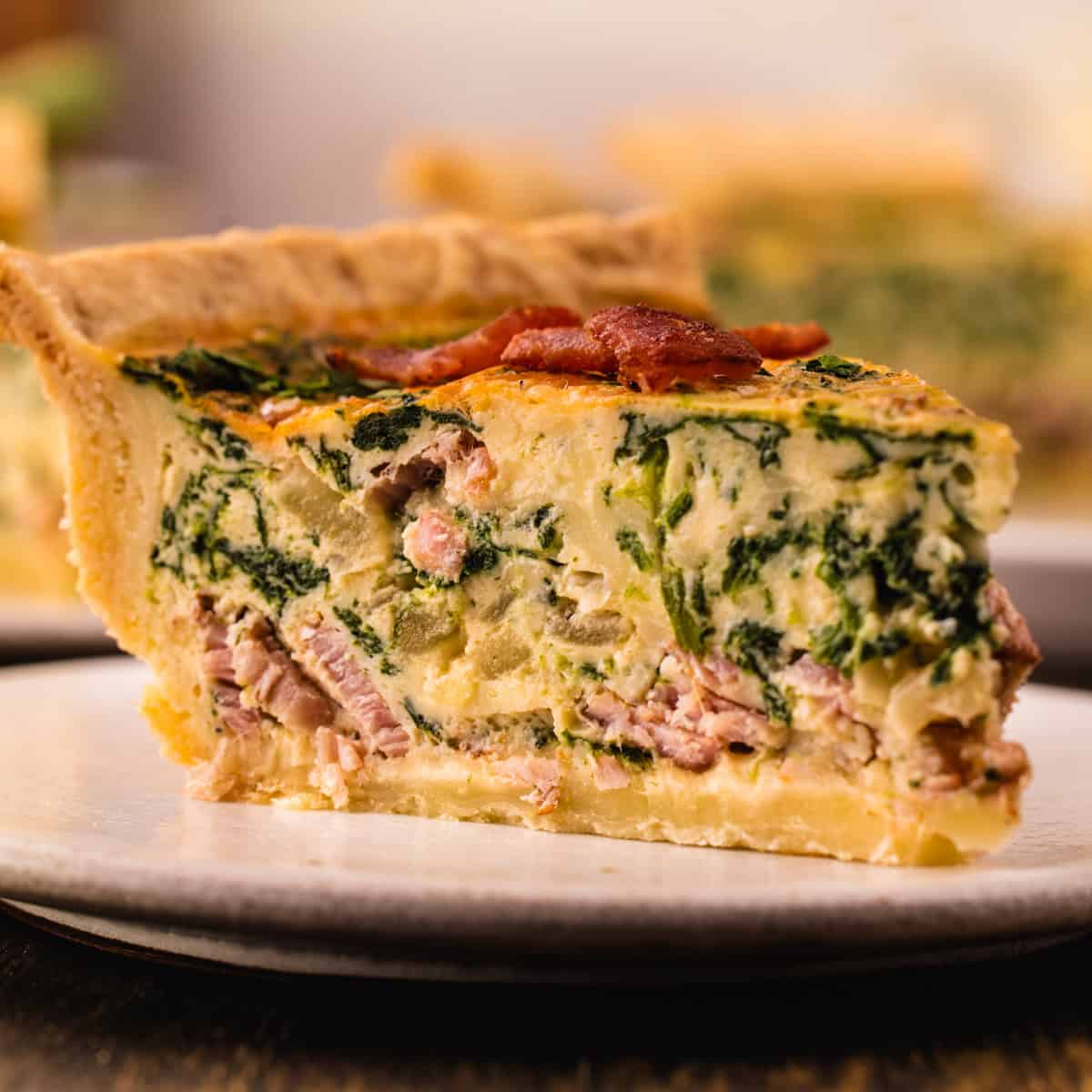 Quiche A slice of quiche filled with spinach, and bacon bits on a plate.