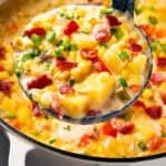 A ladleful of creamy corn and potato chowder topped with bacon bits and chopped green onions.