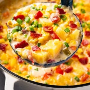 A ladleful of creamy corn and potato chowder topped with bacon bits and chopped green onions.