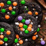 Black chocolate cookies decorated with orange, green, and purple candy-coated chocolates, sprinkles, and edible candy eyes.