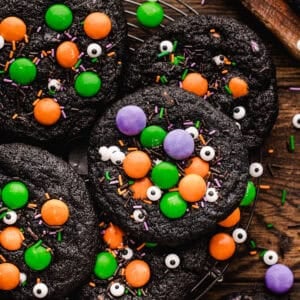 Black chocolate cookies decorated with orange, green, and purple candy-coated chocolates, sprinkles, and edible candy eyes.
