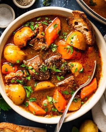 A bowl of beef stew with chunks of meat, potatoes, and carrots, garnished with fresh herbs.