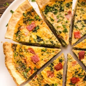 Slices of spinach, cheese, and bacon quiche arranged in a circle on a white plate.