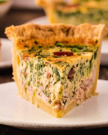 A single slice of spinach and bacon quiche on a white plate.