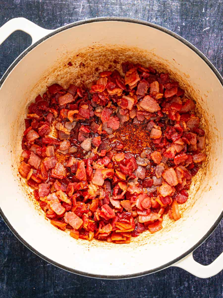 How to Make Corn Chowder (Step-By-Step Photos) Diced bacon frying in a white enameled cast iron pot.