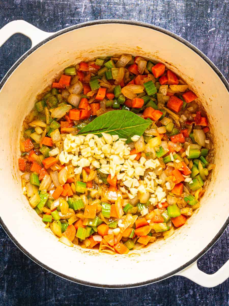 How to Make Corn Chowder (Step-By-Step Photos) A Dutch oven containing sautéed diced carrots, celery, and onions, topped with minced garlic and a bay leaf.