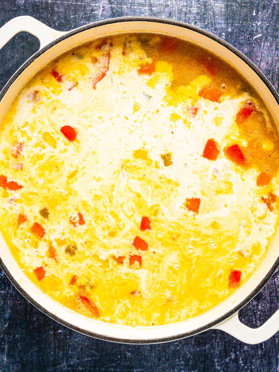 How to Make Corn Chowder (Step-By-Step Photos) A creamy yellow soup with chopped red vegetables in a white Dutch oven.