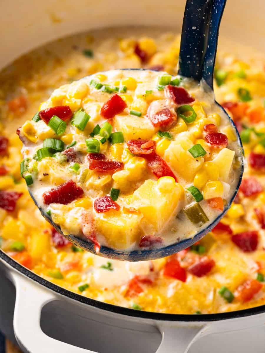 How to Make Corn Chowder (Step-By-Step Photos) A blue ladle scoops creamy corn chowder topped with bacon bits and green onions from a white pot.
