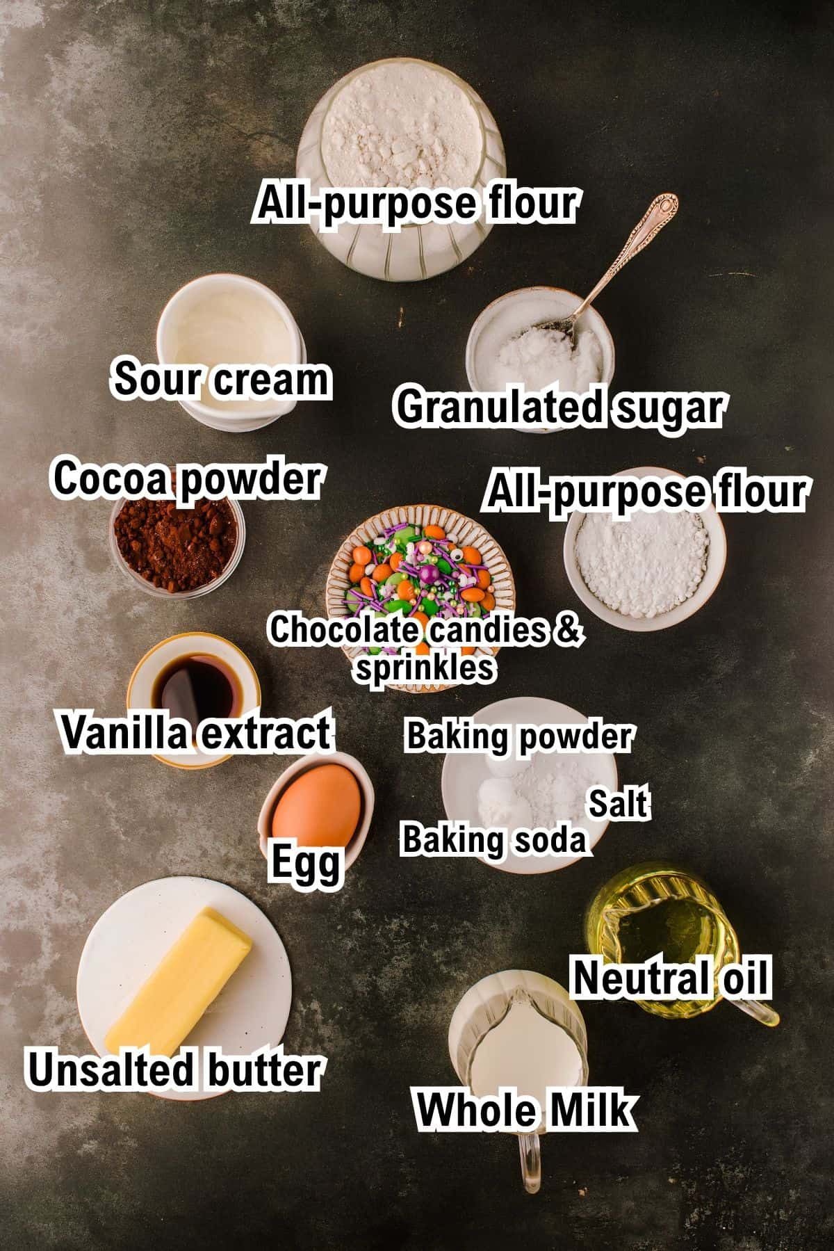 The Ingredients for Halloween Cupcakes This photo shows the ingredients for Halloween Cupcakes: all-purpose flour, sour cream, granulated sugar, cocoa powder, chocolate candies and sprinkles, vanilla extract, baking powder, salt, baking soda, egg, unsalted butter, neutral oil, and whole milk.